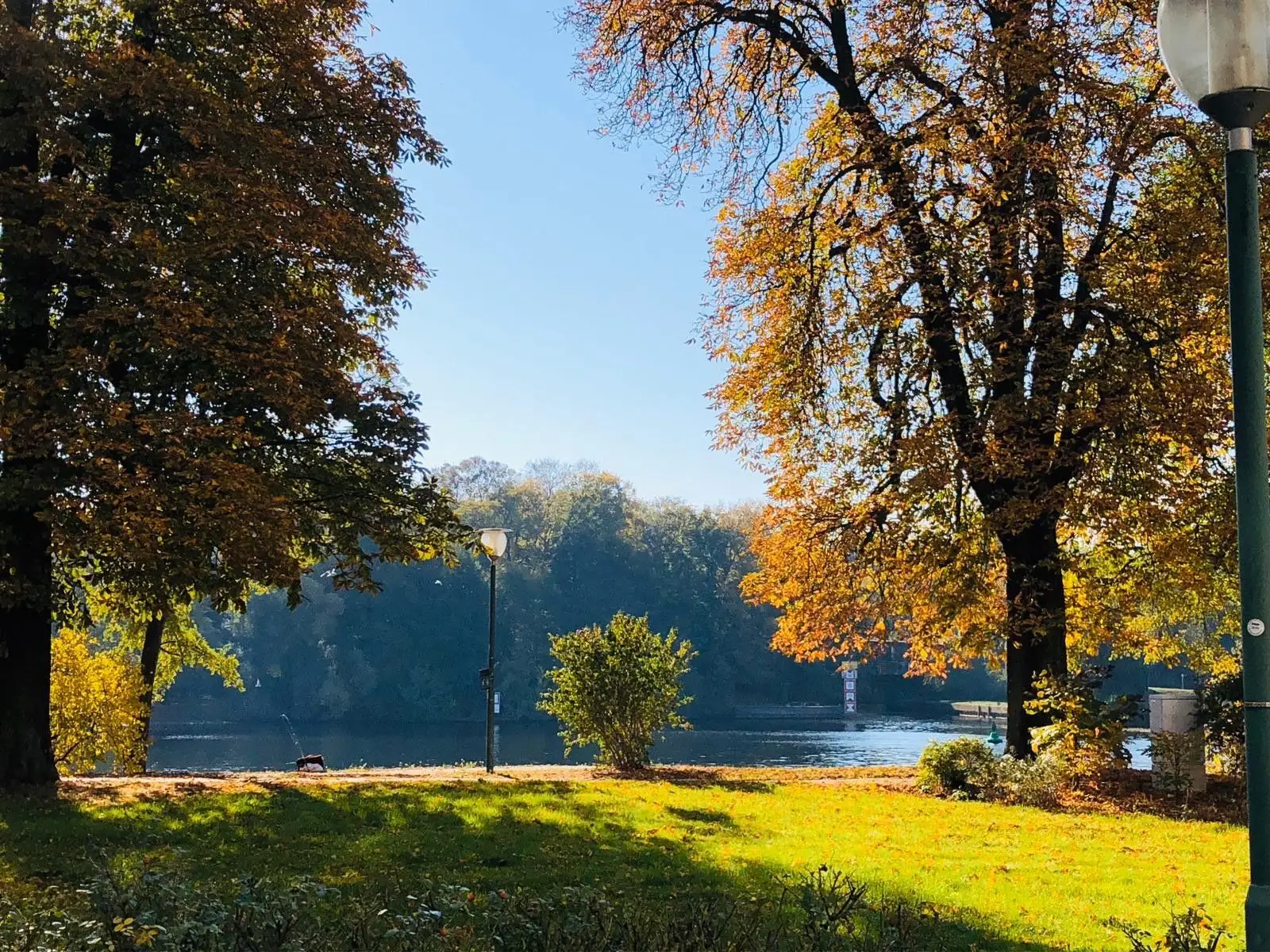 Sonniger Park am Wasser mit Bäumen, Wiese und Blick zur Havel.
