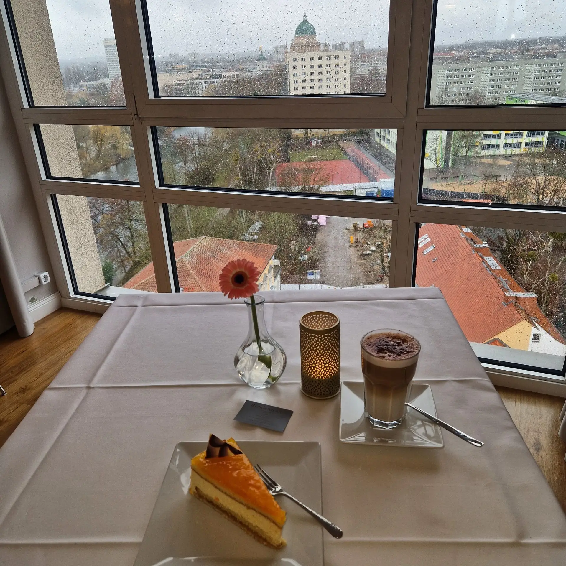 Ein Stück Kuchen und ein Getränk an einem gedeckten Tisch vor dem Fensterblick.