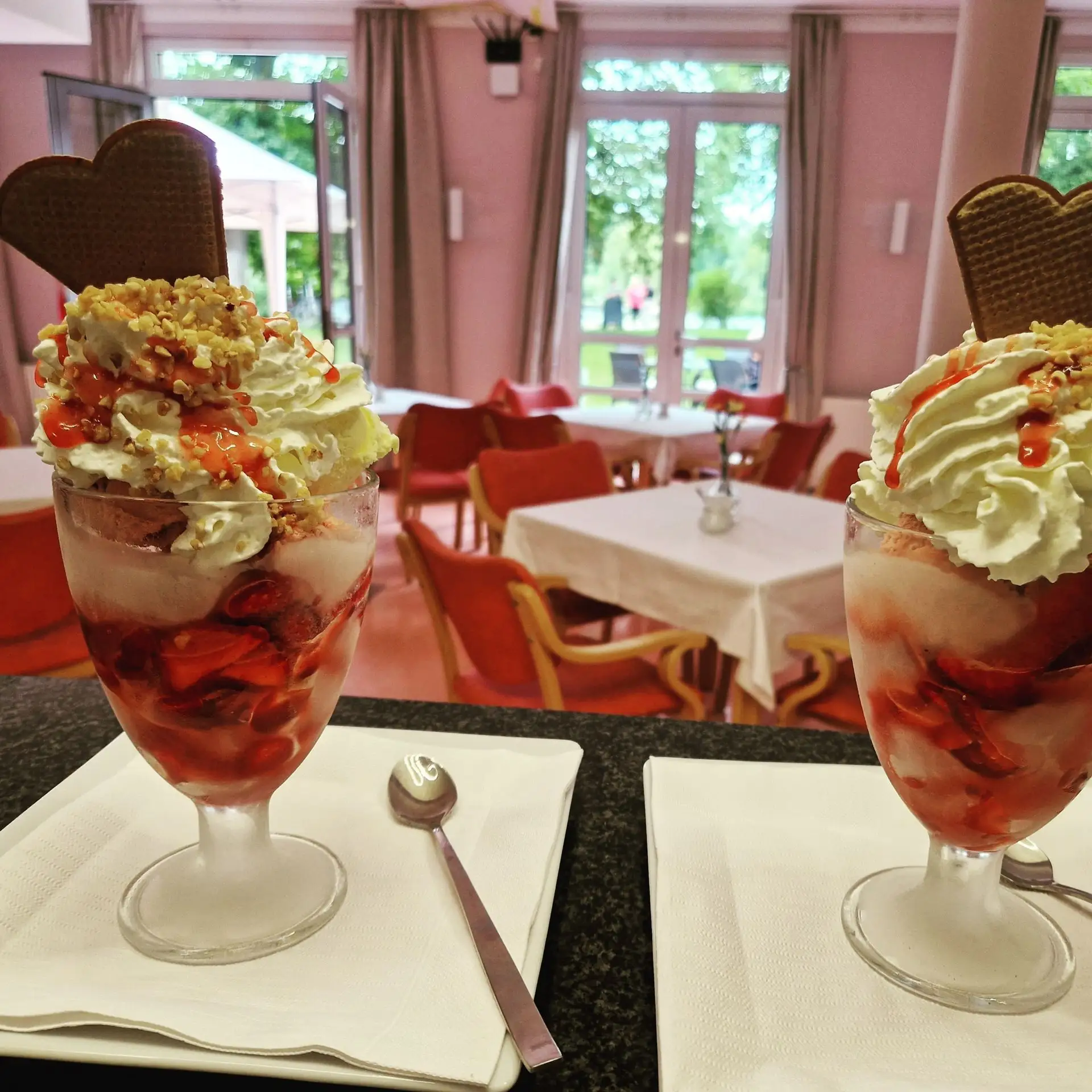 Zwei Eisbecher mit Sahne und Früchten auf einem Tisch im Café.