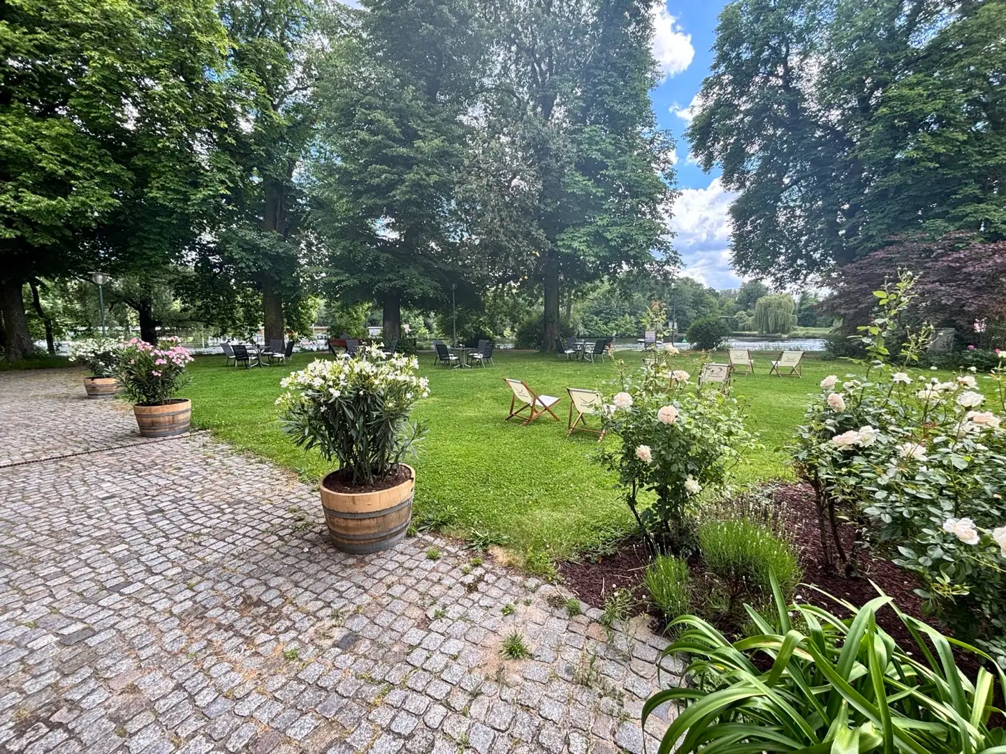 Große Gartenwiese mit Blumen, Liegestühlen, Sitzgruppen und Blick zum Wasser.