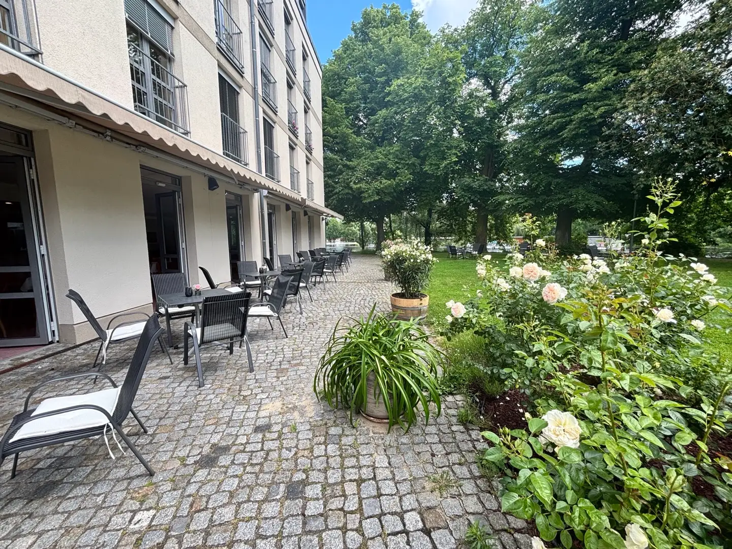 Terrassentische entlang des Residenzgebäudes neben einem blühenden Rosenbeet.