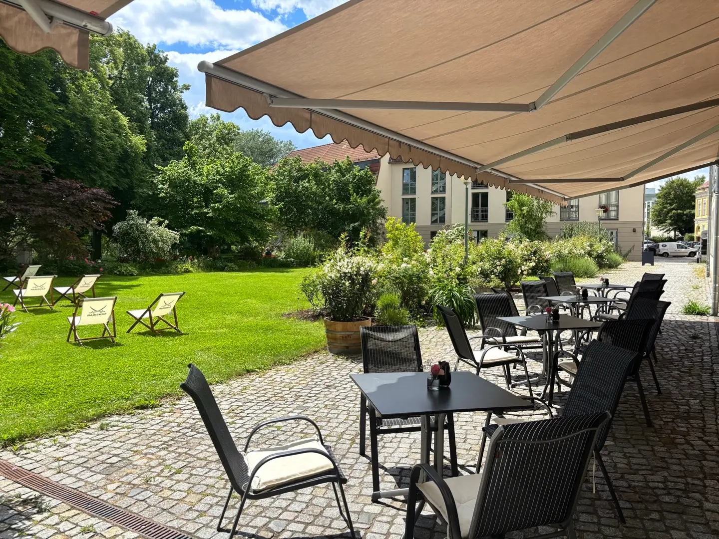 Terrassentische unter einer Markise mit Blick auf den grünen Garten des ResidenzCafés.